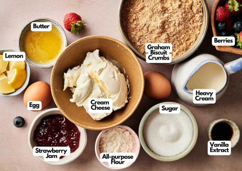 Assorted mini cheesecakes ingredients labeled in bowls and cups, including cream cheese, graham cracker crumbs, sugar, butter, lemon, egg, heavy cream, vanilla extract, flour, jam, and berries.
