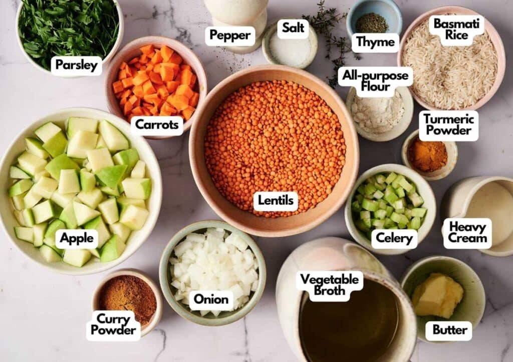 Bowls containing labeled ingredients for Mulligatawny Soup, including lentils, apple, carrots, parsley, onion, celery, basmati rice, vegetable broth, heavy cream, butter, and a blend of spices.