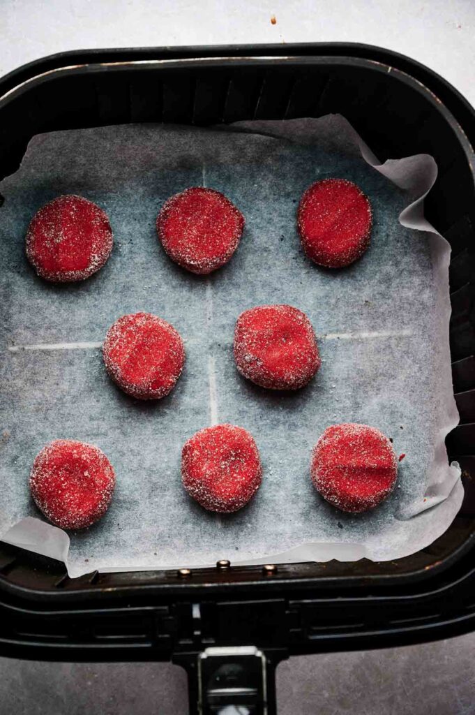 Eight red, sugar-coated Air Fryer Strawberry Cookies are arranged on parchment paper inside an air fryer basket.