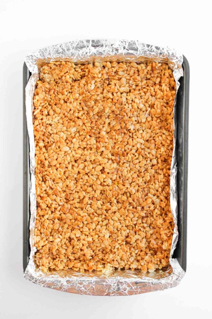 A baking tray lined with foil, filled with a pressed mixture of Butterscotch Rice Treats, ready to be sliced into delicious squares.