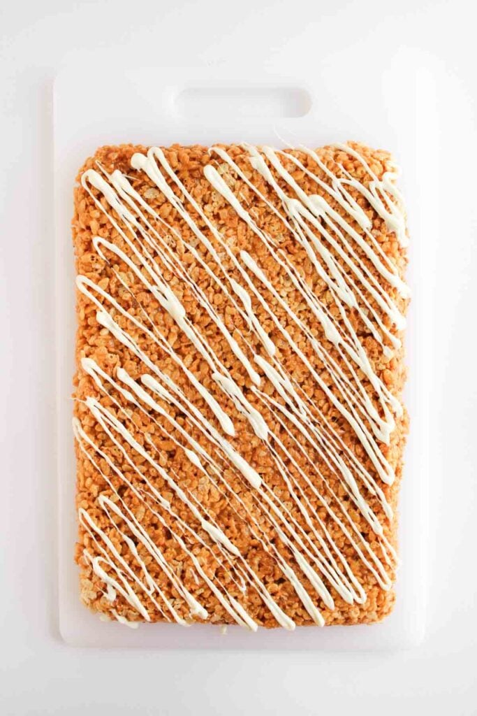 A large rectangular Butterscotch Rice Treat with white icing drizzled on top, placed on a white cutting board.