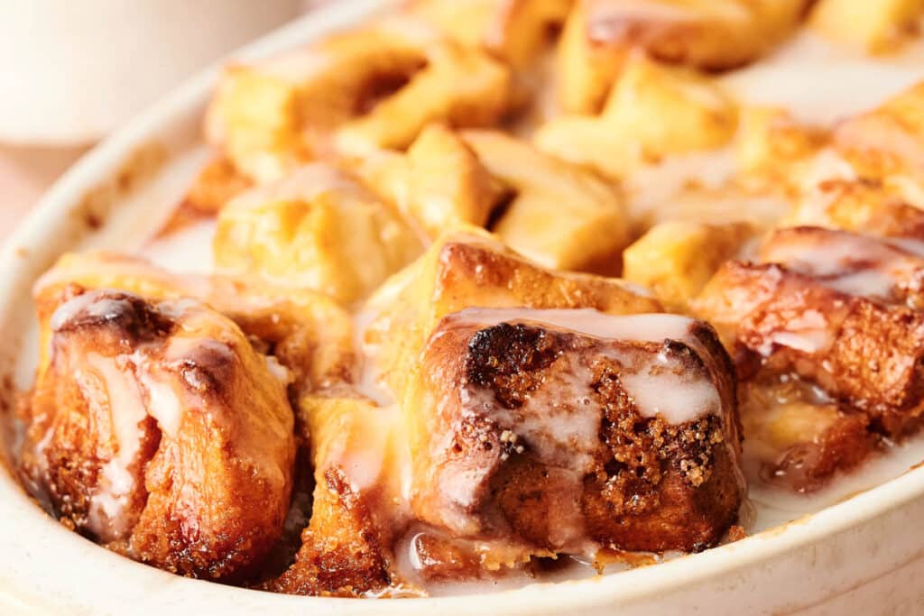 Close-up of Air Fryer Cinnamon Roll Casserole pieces topped with icing in a white baking dish.