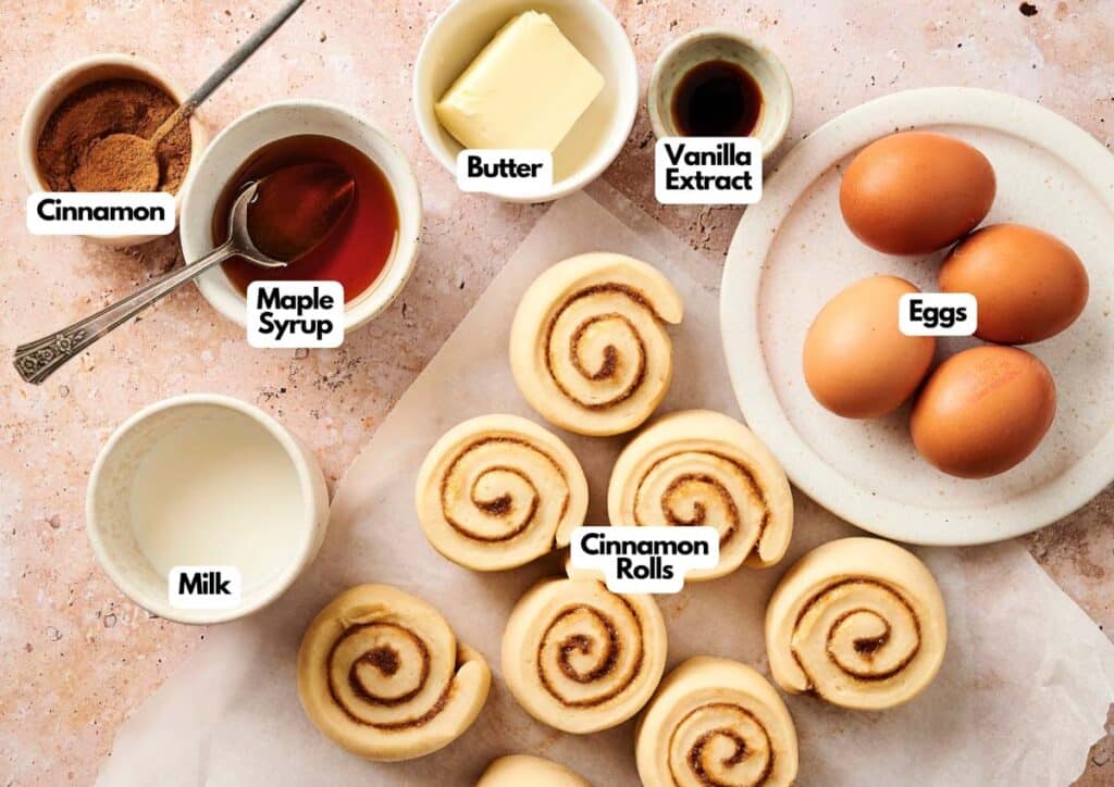Ingredients for Air Fryer Cinnamon Roll Casserole displayed on a countertop: butter, vanilla extract, eggs, milk, cinnamon, maple syrup, and uncooked cinnamon roll spirals.
