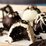 A close-up of chocolate truffles, including Oreo Balls, some coated in white chocolate and some in dark, with one truffle in front showing a bite taken out.