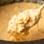 A close-up of a spoon lifting creamy Slow Cooker Mac and Cheese out of a pot.