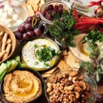 A festive Veggie Christmas Charcuterie Board featuring hummus, labneh, dips, nuts, grapes, cucumber sticks, breadsticks, mozzarella balls, red peppers, and crackers adorned with holiday greenery.