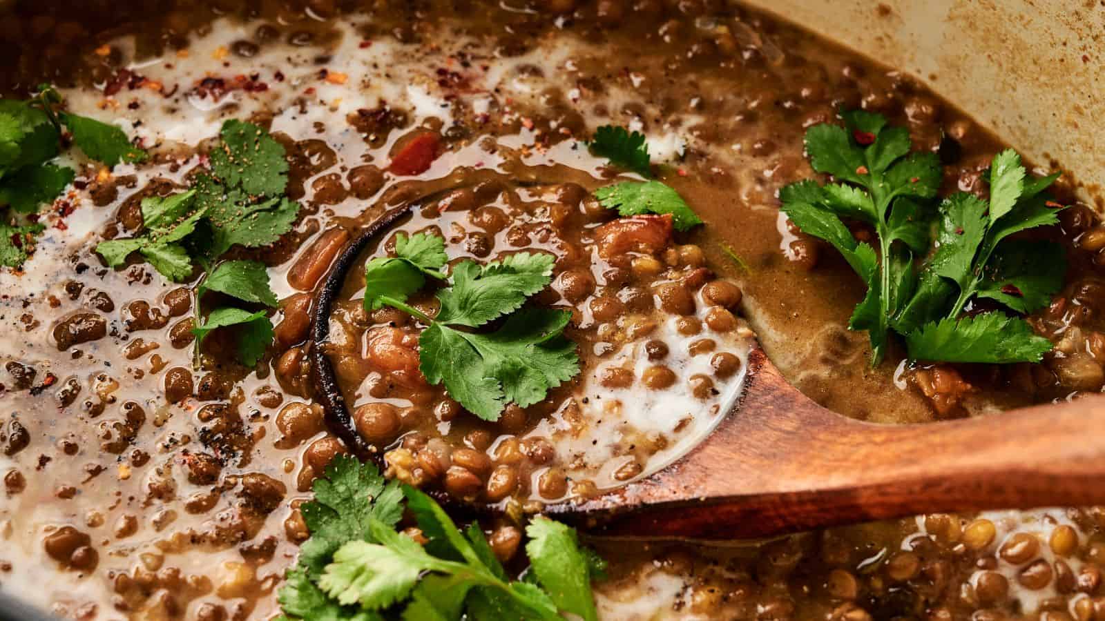A pot of lentil stew with cilantro garnish and a wooden spoon.