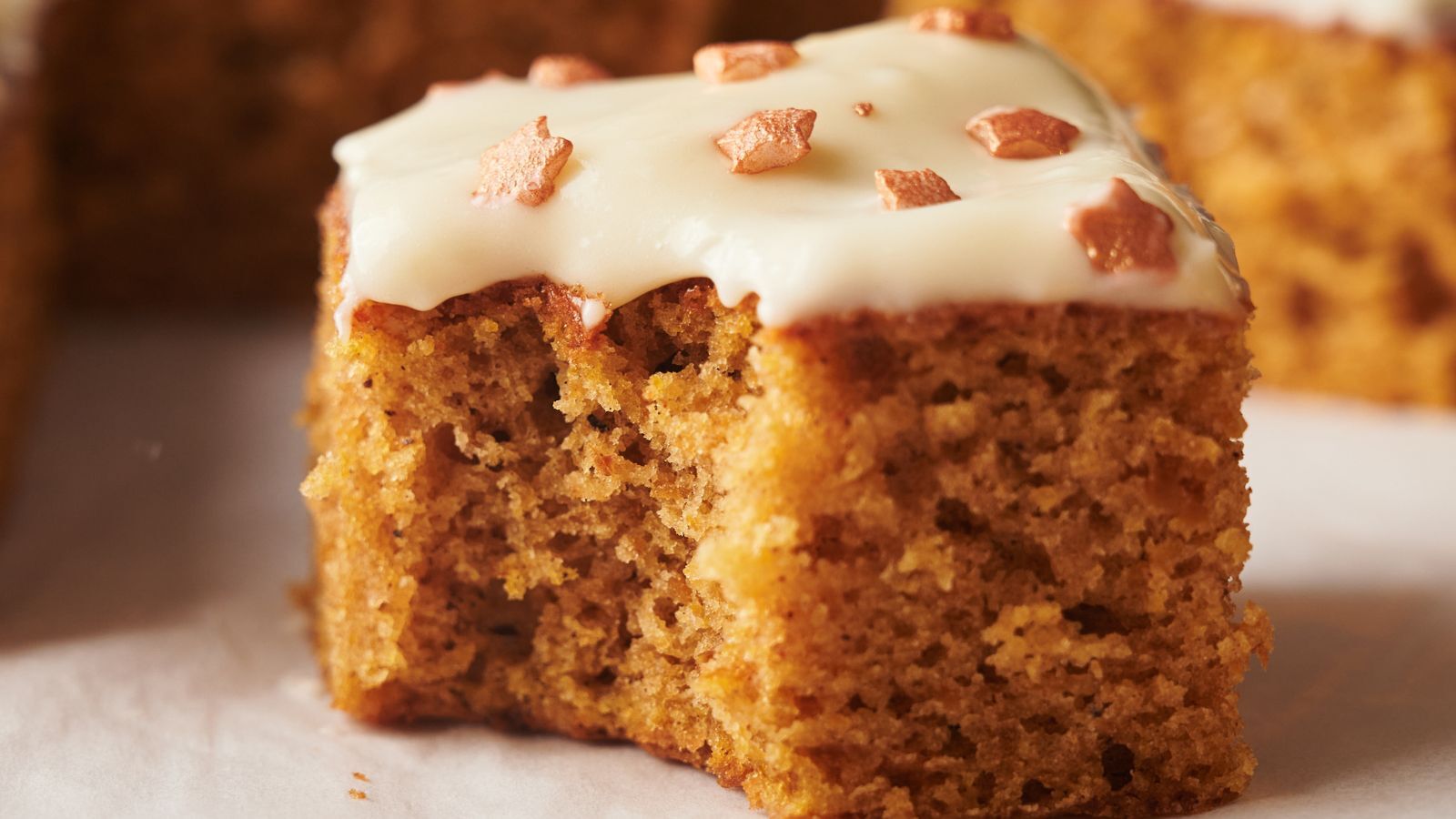 A close-up of a slice of spiced cake topped with white icing and small decorative sprinkles.