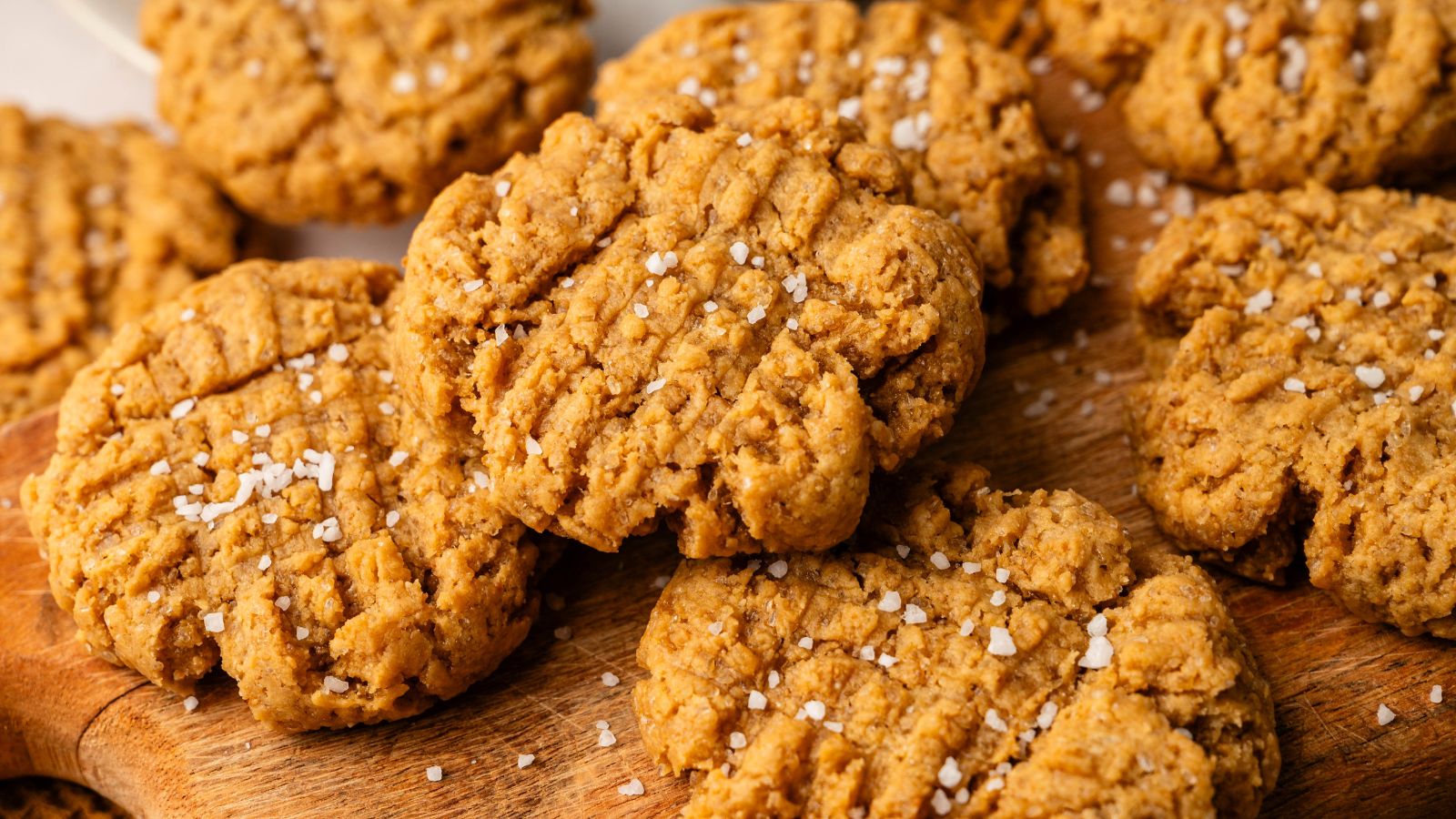 Several peanut butter cookies topped with coarse salt are arranged on a wooden surface.