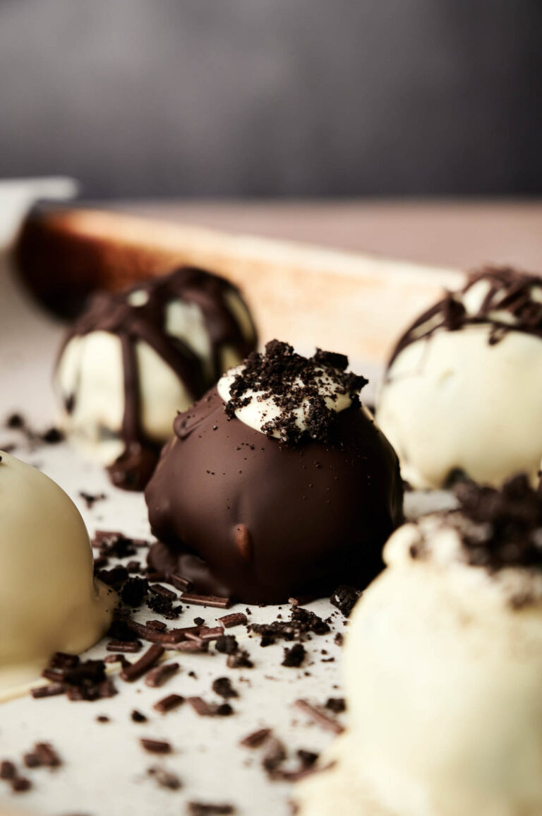 Close-up of assorted chocolate-covered truffles, including Oreo Balls topped with crushed cookies and chocolate drizzle, displayed on a light surface.