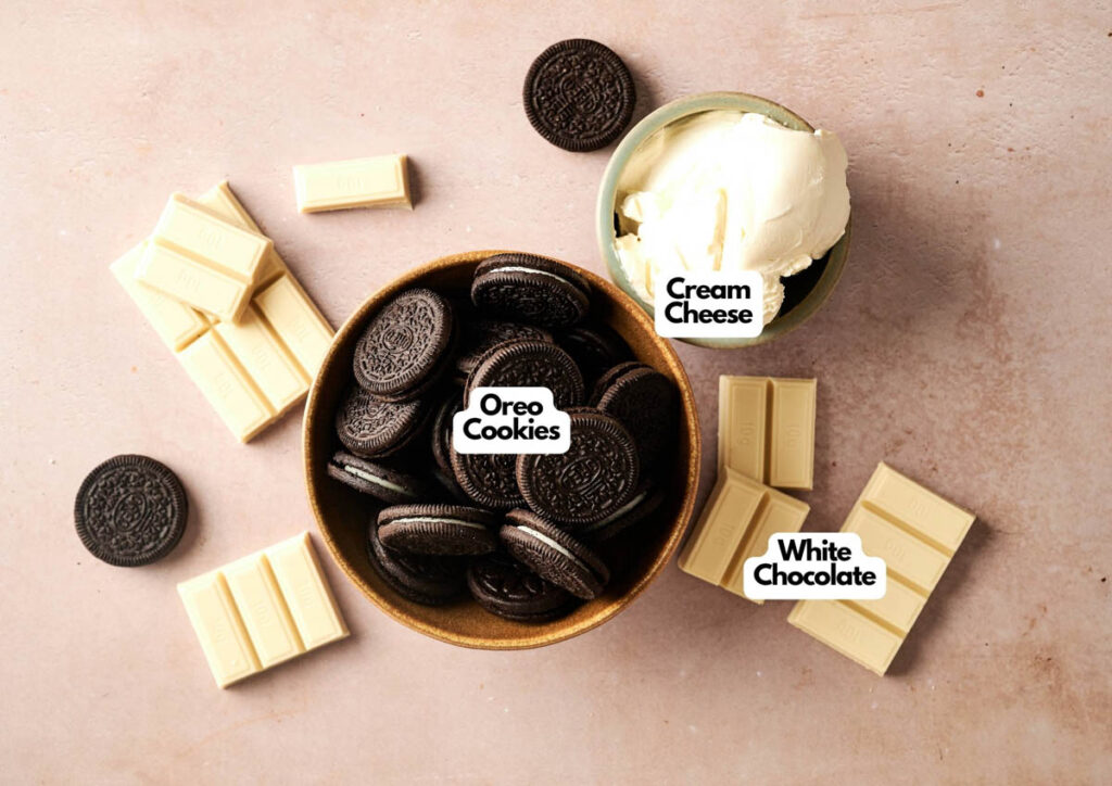 A bowl of Oreo cookies, blocks of white chocolate, and a scoop of cream cheese arranged on a light surface—these are the key ingredients for delicious Oreo Balls, each labeled accordingly.