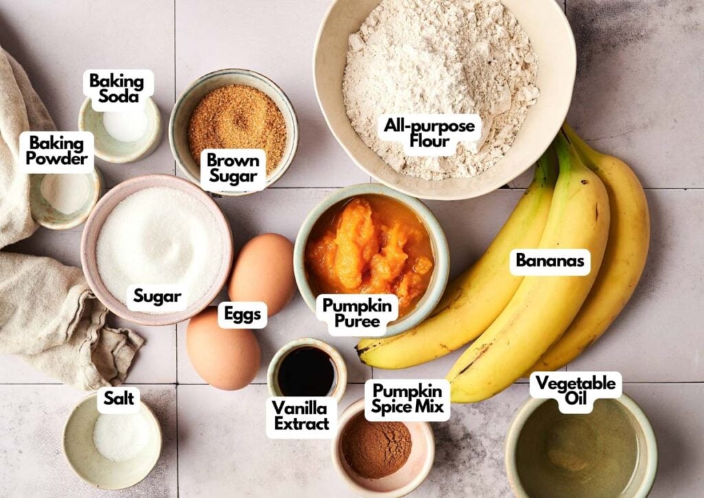 Top-down view of Pumpkin Banana Bread ingredients, including eggs, bananas, flour, sugars, baking powder, baking soda, salt, vanilla extract, pumpkin puree, pumpkin spice mix, and vegetable oil.