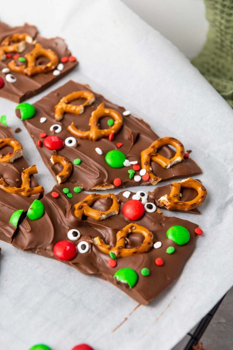 Reindeer Chocolate Bark topped with pretzels, red and green candies, googly eye decorations, and colorful sprinkles on parchment paper.