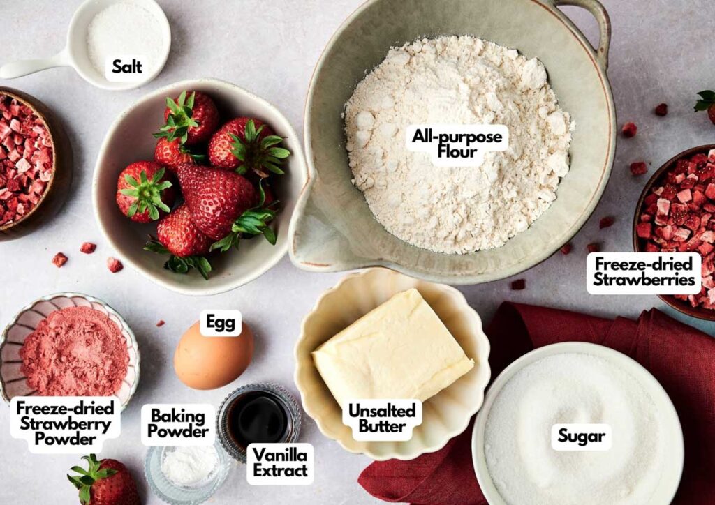 Baking ingredients arranged on a table, including all-purpose flour, sugar, salt, egg, unsalted butter, vanilla extract, baking powder, strawberries, and freeze-dried strawberries&mdash;perfect for making Air Fryer Strawberry Cookies.