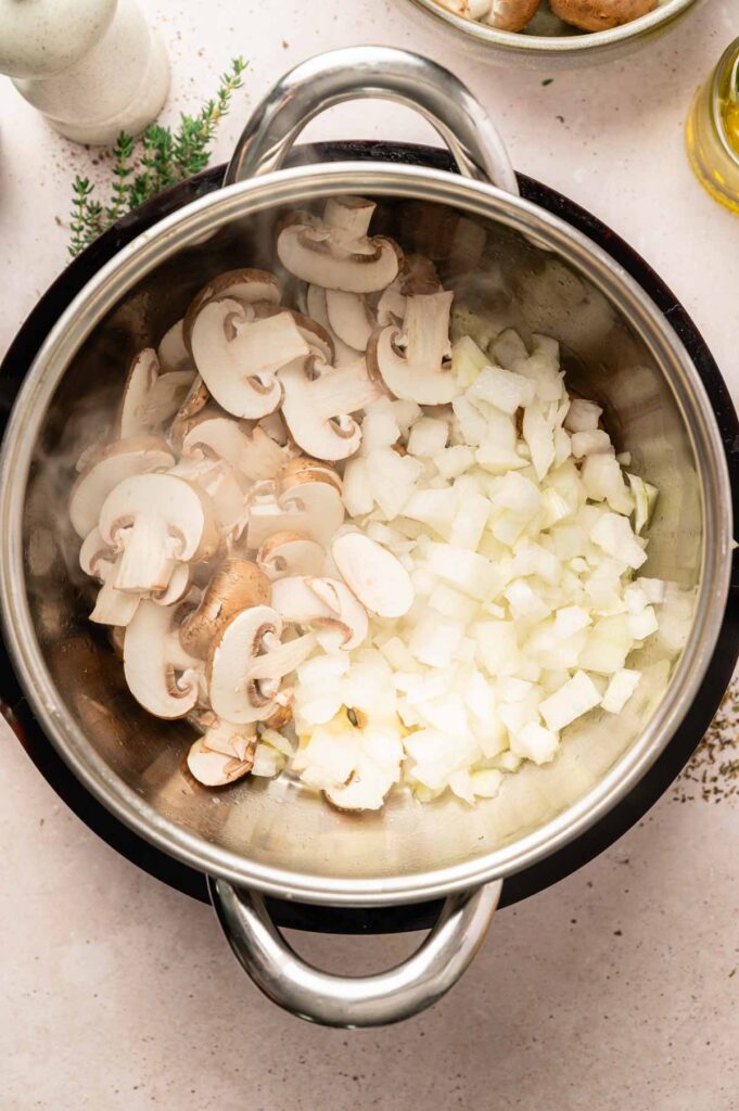 Sliced mushrooms and diced onions sit in a steaming pot, ready to be sautéed together.