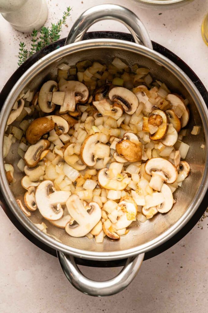 Mushrooms, onions, and garlic cook down together in a pot until softened and lightly golden at the edges.
