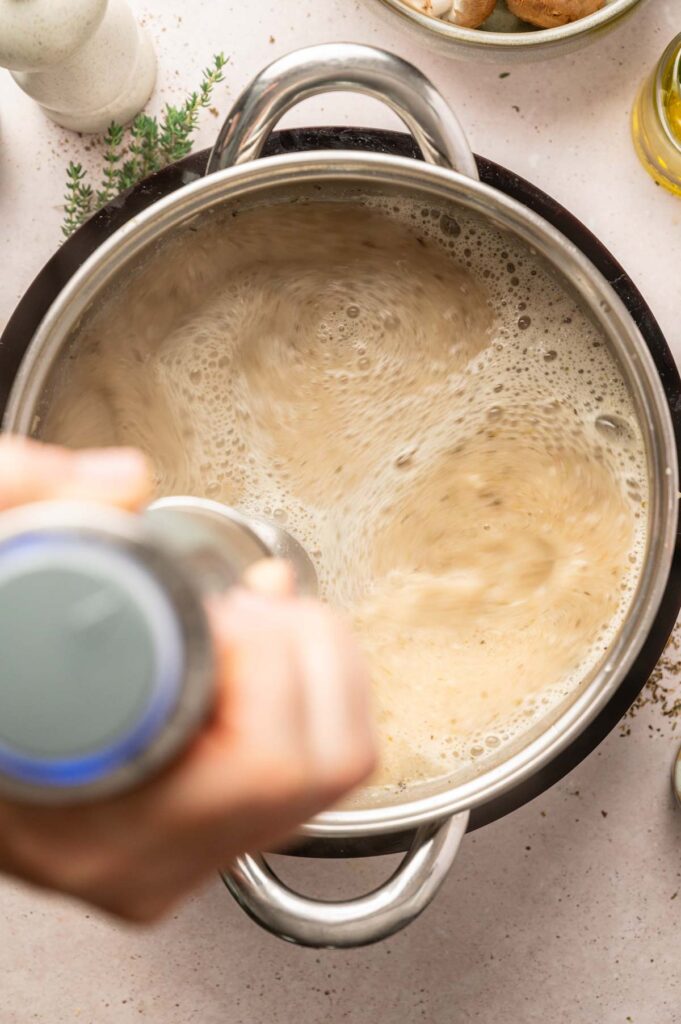 A hand blends the gravy directly in the pot, smoothing out the mushrooms into a lump-free sauce.