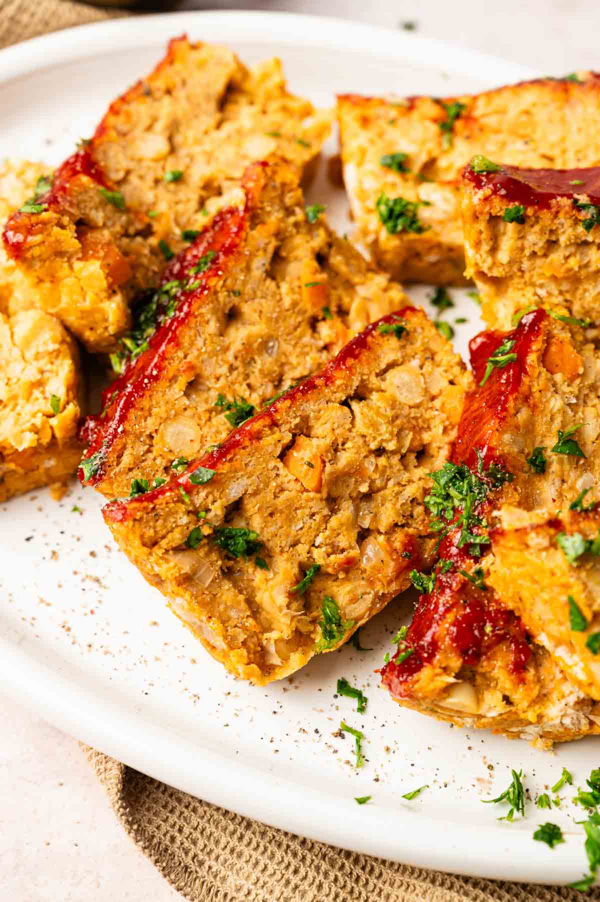 Slices of Vegetarian Meatloaf made from chickpeas, topped with ketchup glaze and garnished with chopped parsley on a white plate.
