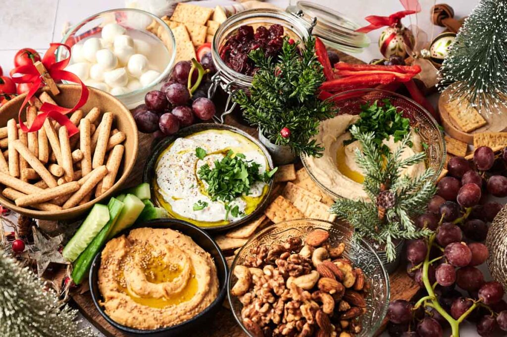 Colorful vegetarian holiday charcuterie board with assorted cheeses, fresh vegetables, fruits, nuts, and festive dips