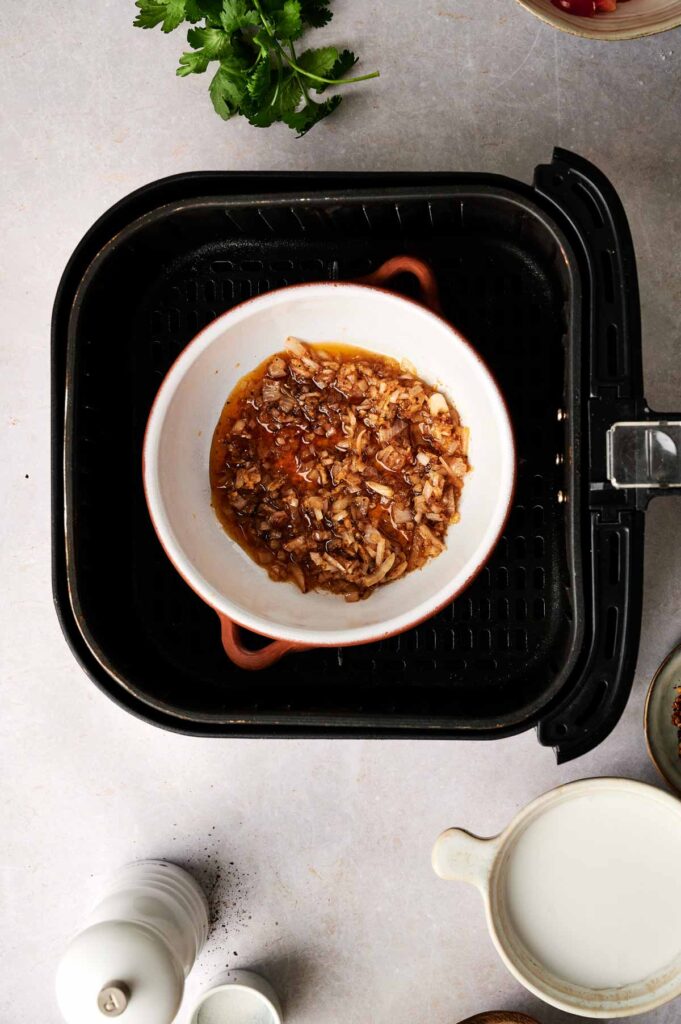 Softened aromatics and spices cooking in a small dish, building the flavor base for lentil soup.
