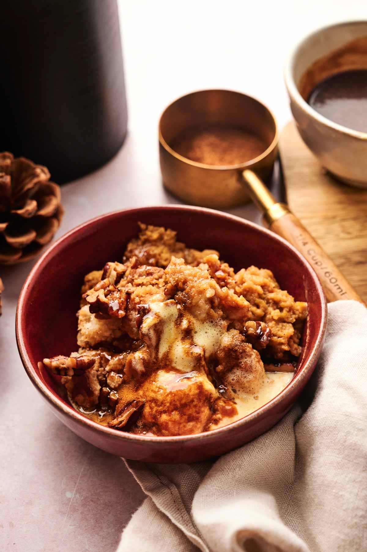 A bowl of apple crisp topped with melting vanilla ice cream sits on a table, alongside a measuring cup, a bowl, and a napkin&mdash;perfect for fall desserts like Air Fryer Pumpkin Dump Cake.