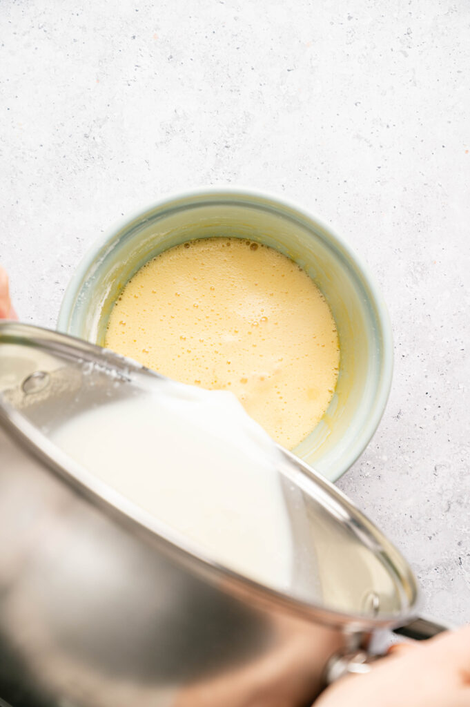 Warm milk mixture is poured into whisked egg yolks to temper them for the pastry cream.