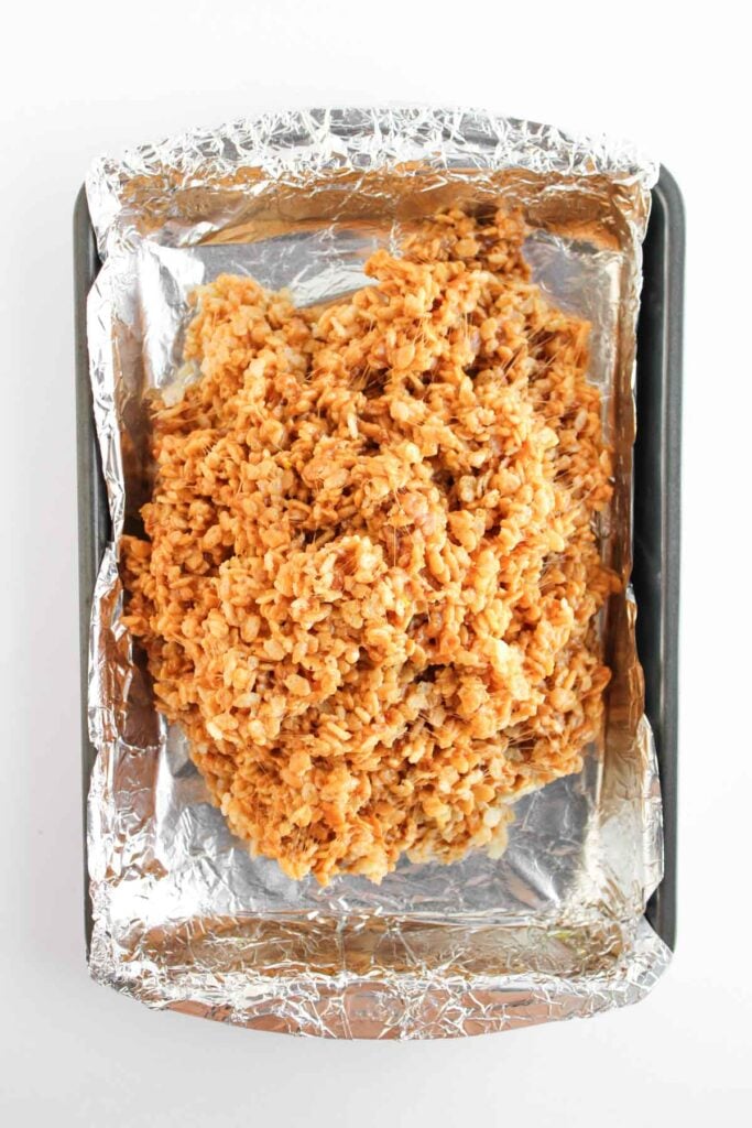 The butterscotch rice cereal mixture is pressed into a foil-lined pan, ready to cool and set.