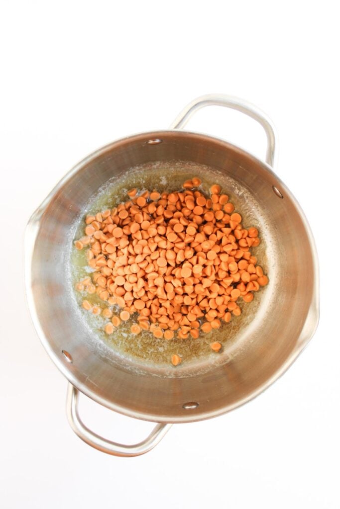 Butterscotch morsels are added to melted butter in a stainless steel pot, ready to be stirred until smooth and glossy.
