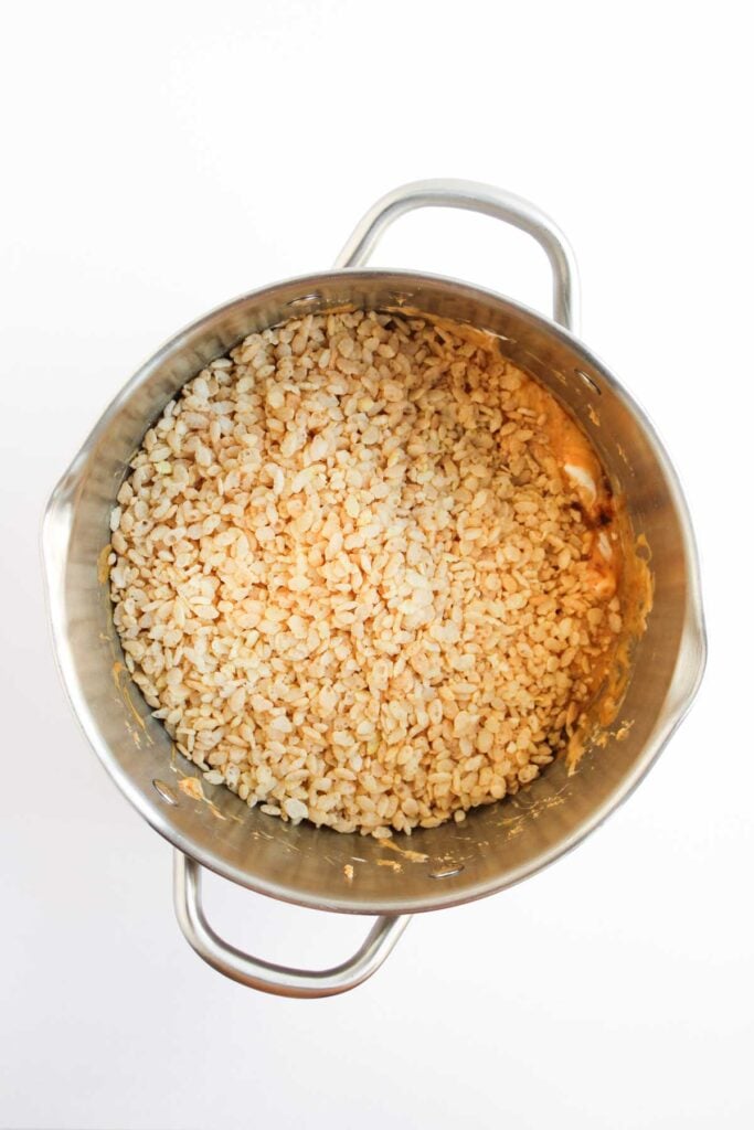 Rice cereal is folded into the melted butterscotch marshmallow mixture until every piece is evenly coated.