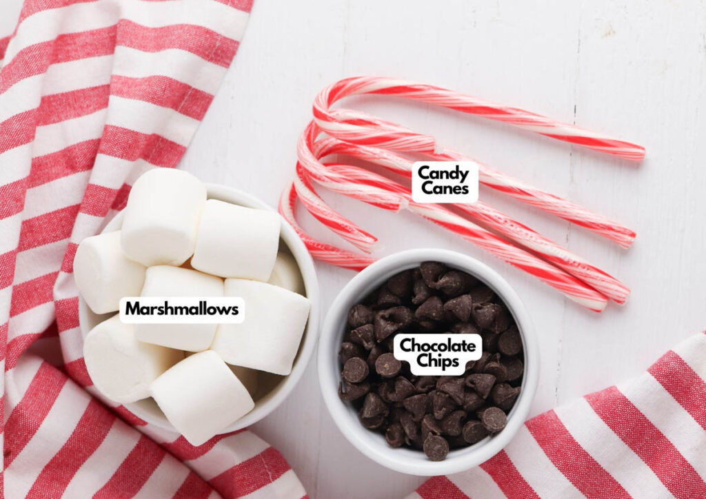 Three labeled bowls display marshmallows, chocolate chips, and candy canes on a white surface with a red-and-white striped cloth&mdash;perfect for making Candy Cane Hot Chocolate Stirrers.