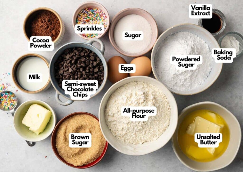Bowls containing baking ingredients&mdash;perfect for a Cookie Cake&mdash;including cocoa powder, sprinkles, sugar, powdered sugar, baking soda, vanilla extract, all-purpose flour, unsalted butter, brown sugar, milk, eggs, and chocolate chips.