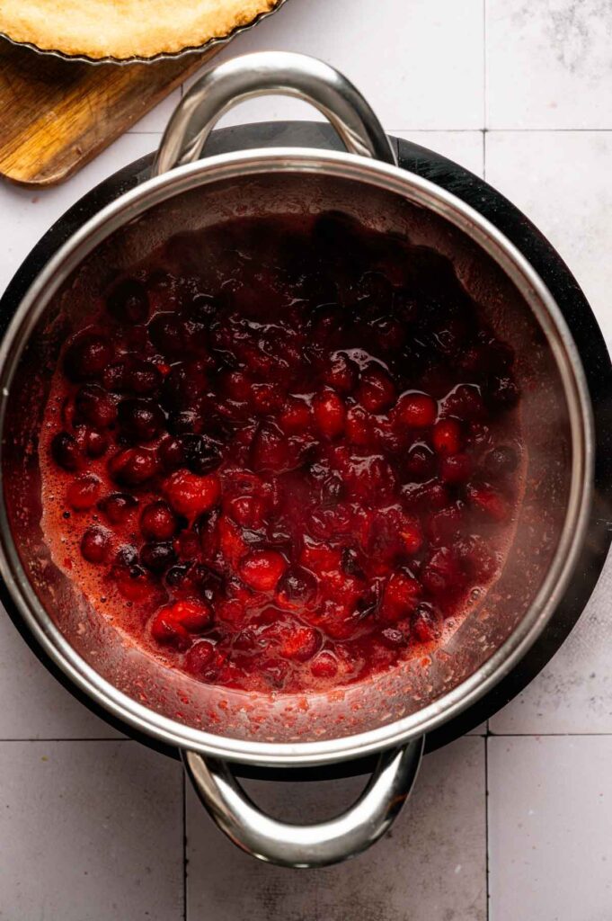 A pot of simmering cranberry filling sits on a stovetop, with visible whole cranberries and thick red sauce—perfect for creating a luscious Cranberry Curd Tart.