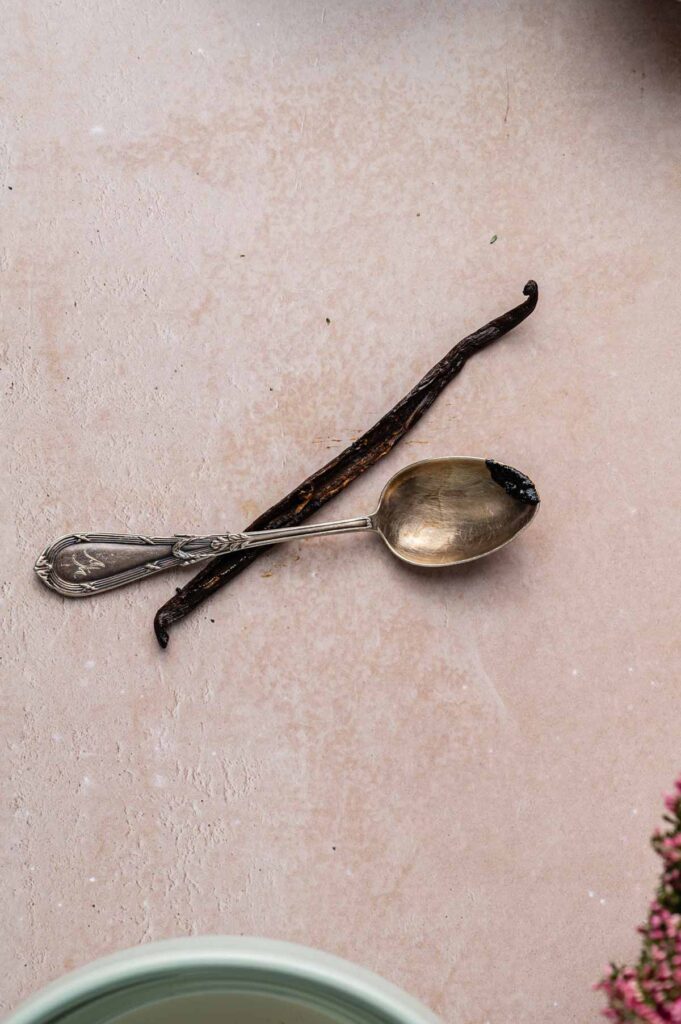 Crème brûlée ingredient shot with a split vanilla bean and vintage spoon holding scraped vanilla paste.