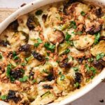An Air Fryer Brussels Sprouts Casserole topped with melted cheese, crispy onions, and chopped parsley, served in a white oval dish.