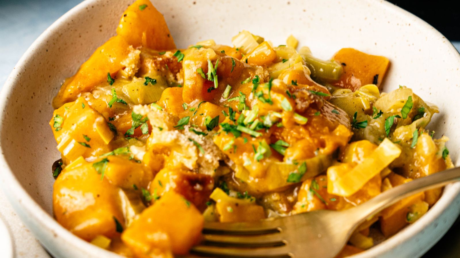 A bowl of baked macaroni and cheese with visible herbs, sauce, and pasta, served with a fork.