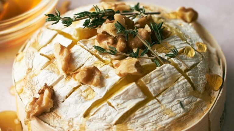 A round of baked brie cheese topped with walnuts, fresh herbs, and drizzled honey.