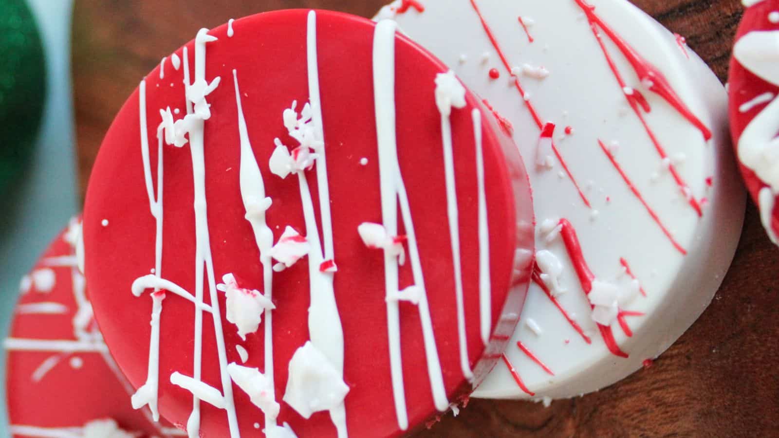 Two round cookies, one red and one white, are decorated with white icing drizzles and white sprinkles, placed on a wooden surface.