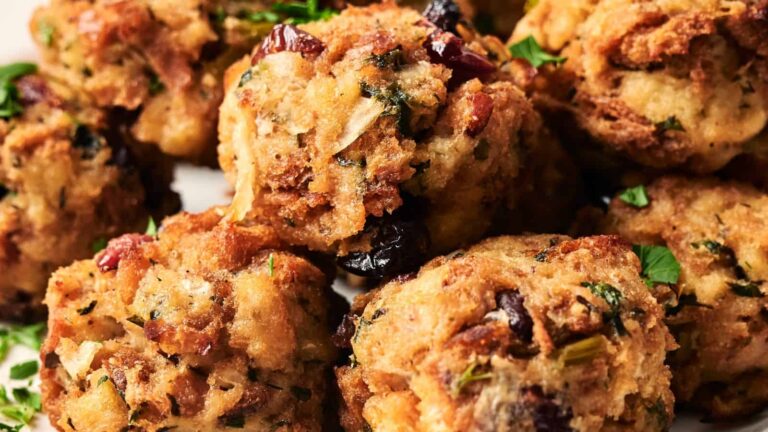 Close-up of several golden-brown stuffing balls with visible herbs, bread pieces, and cranberries.