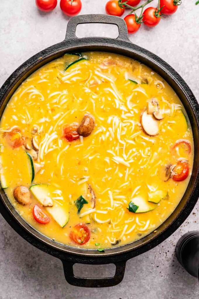 Egg mixture is poured over cooked mushrooms, zucchini, and tomatoes in a cast-iron skillet, just starting to set at the edges.