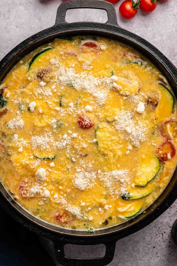 Grated Parmesan is sprinkled over the egg and vegetable mixture in a skillet, ready to go into the oven.