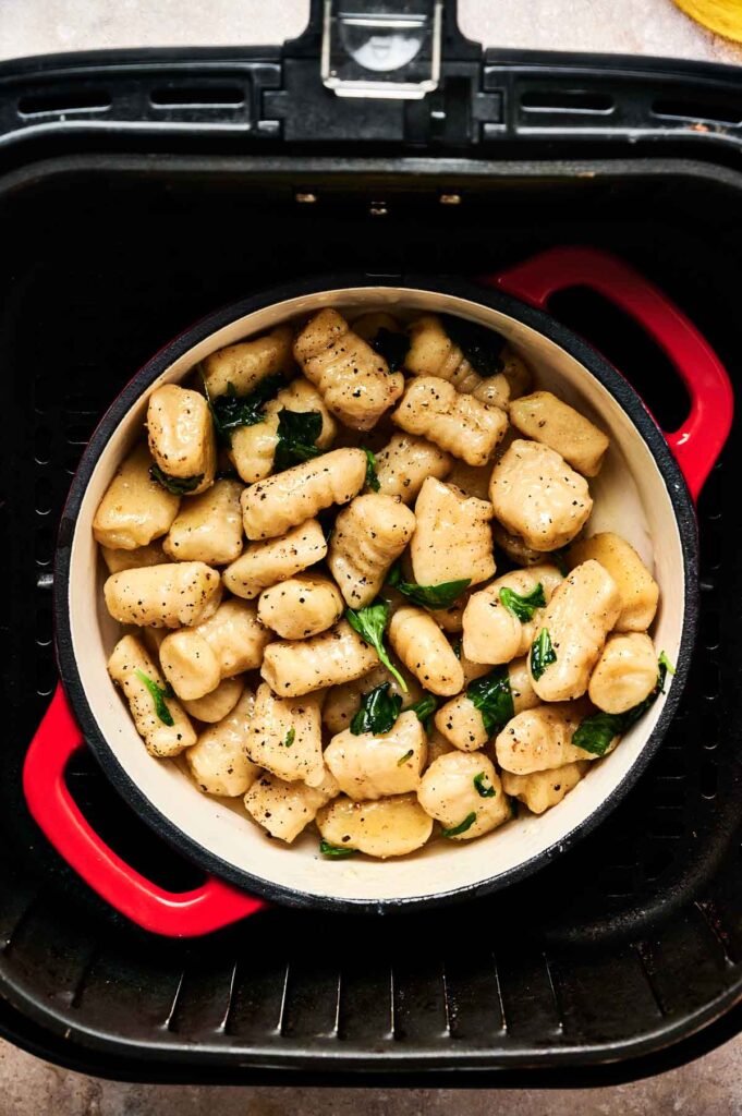 A round dish filled with cooked Air Fryer Gnocchi and spinach sits inside an air fryer basket.