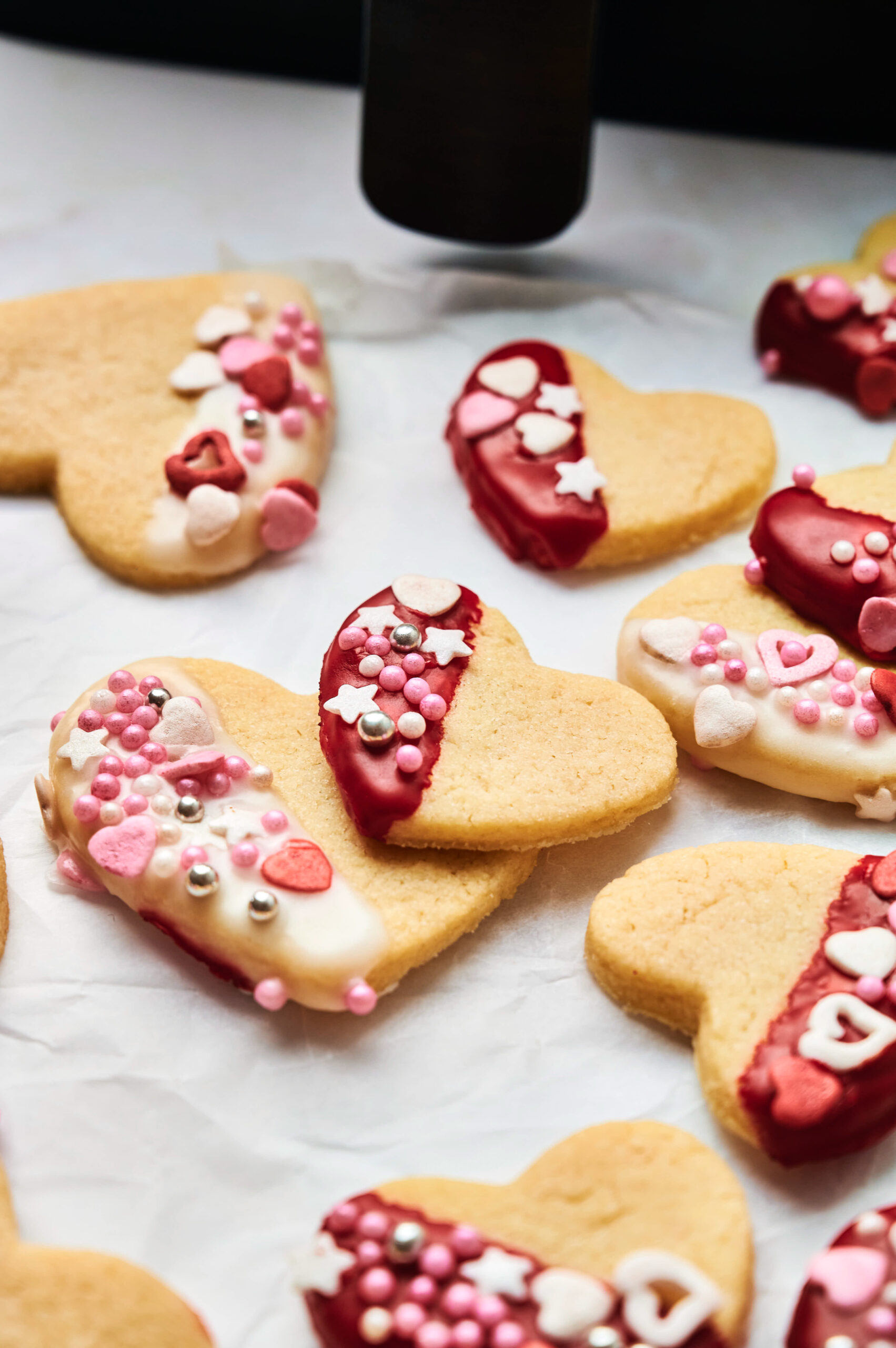 Air Fryer Heart Shaped Cookies decorated with red, white, and pink icing plus assorted sprinkles, arranged beautifully on parchment paper.