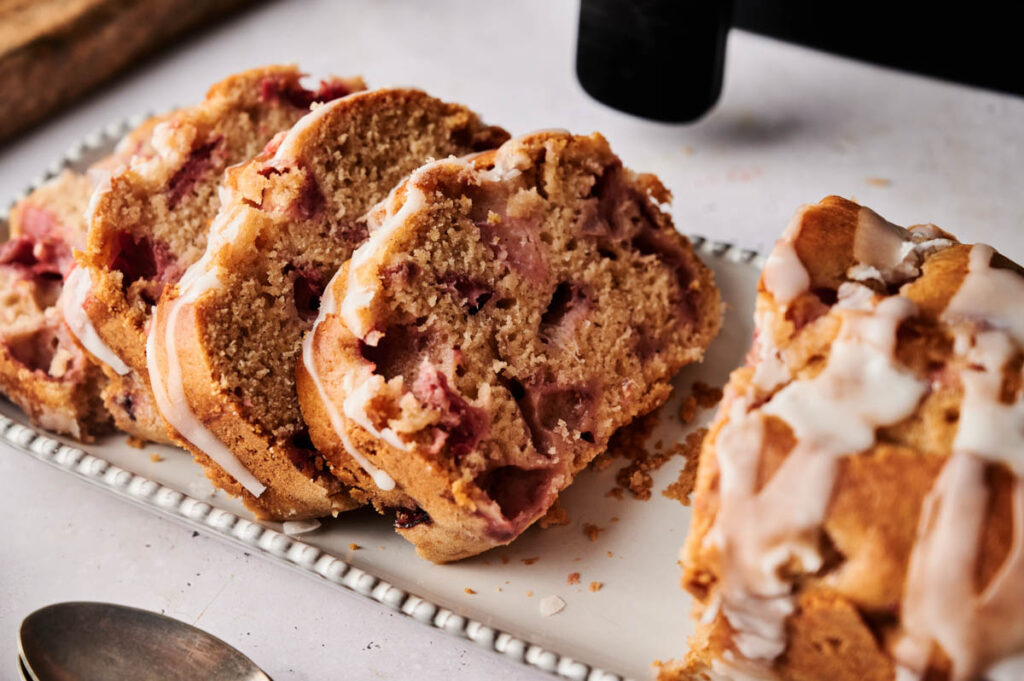 Sliced Air Fryer Strawberry Bread with icing on a rectangular white plate, viewed from above on a light surface.