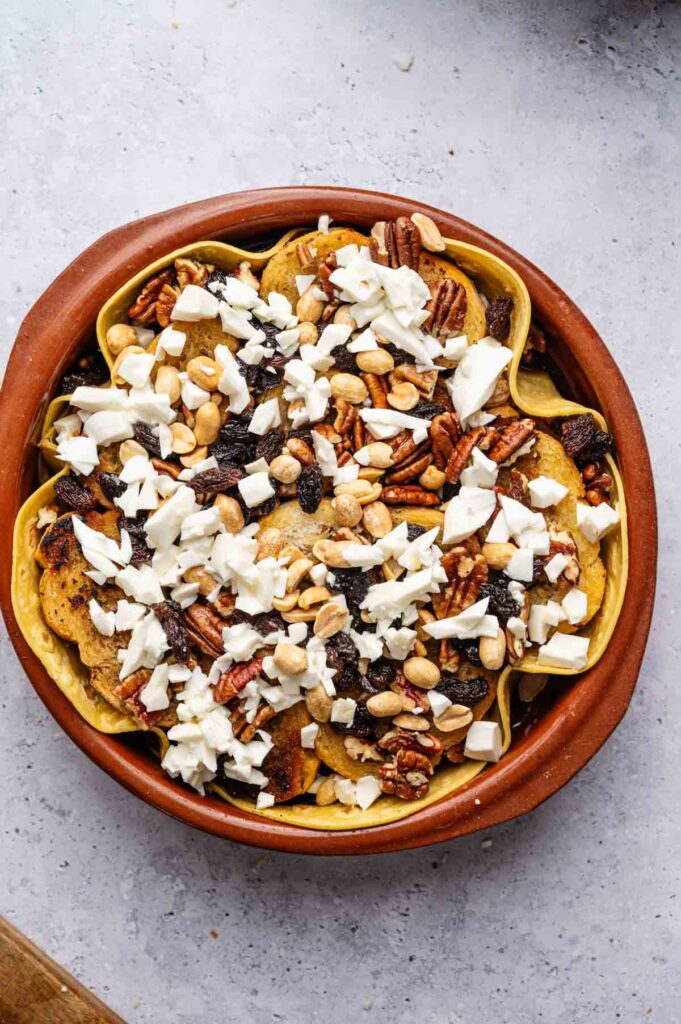 Crumbled queso fresco, pecans, peanuts, and raisins are layered over the fried bread in a clay dish, ready for syrup.
