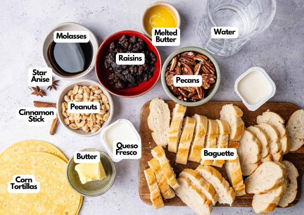 Various labeled ingredients for Capirotada, including corn tortillas, butter, queso fresco, baguette slices, peanuts, cinnamon stick, star anise, molasses, raisins, pecans, melted butter, and water.