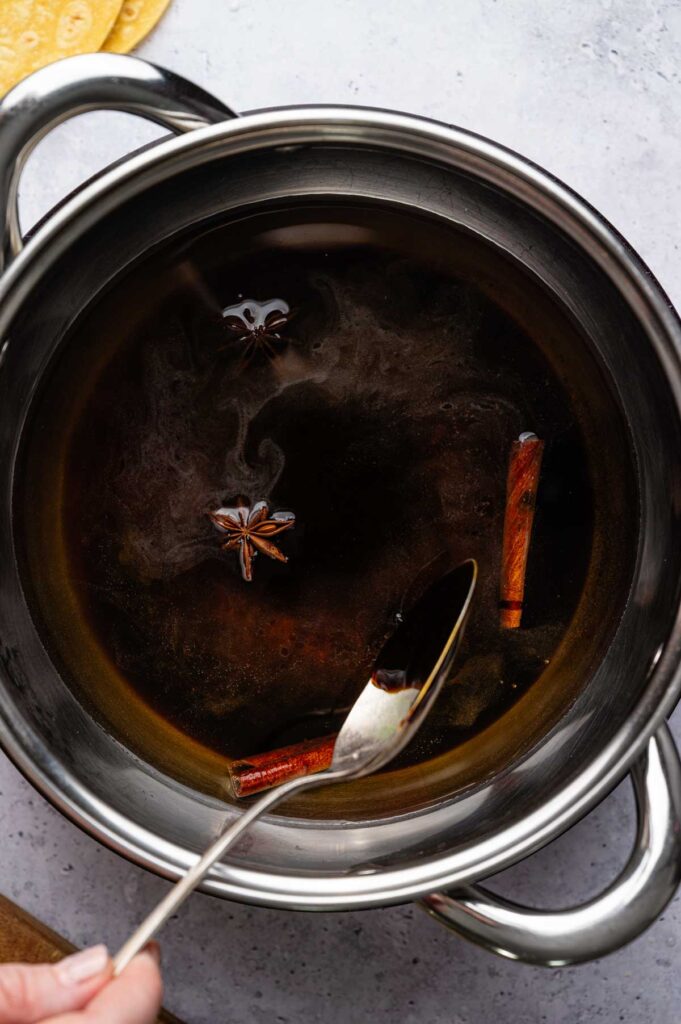 Cinnamon sticks and star anise steep in a saucepan of molasses syrup, simmering until fully dissolved.
