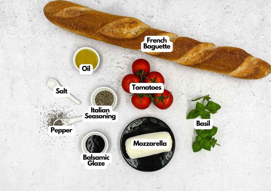A Caprese Appetizer featuring a French baguette, tomatoes, mozzarella, basil, oil, salt, pepper, Italian seasoning, and balsamic glaze arranged on a white surface.