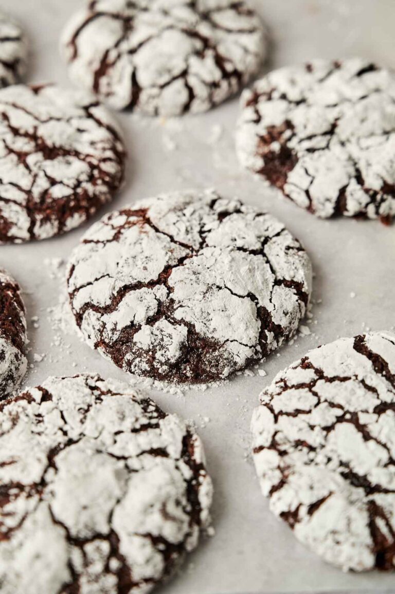 Chocolate Crinkle Cookies covered with powdered sugar are arranged on a sheet of parchment paper, showcasing their classic crackled appearance.