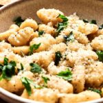 A bowl of Air Fryer Gnocchi topped with grated cheese, chopped parsley, and black pepper.
