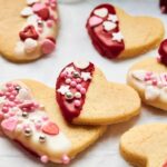Air Fryer Heart Shaped Cookies decorated with white and red icing, pink and white sprinkles, plus tiny candy hearts and stars, arranged on white parchment paper.